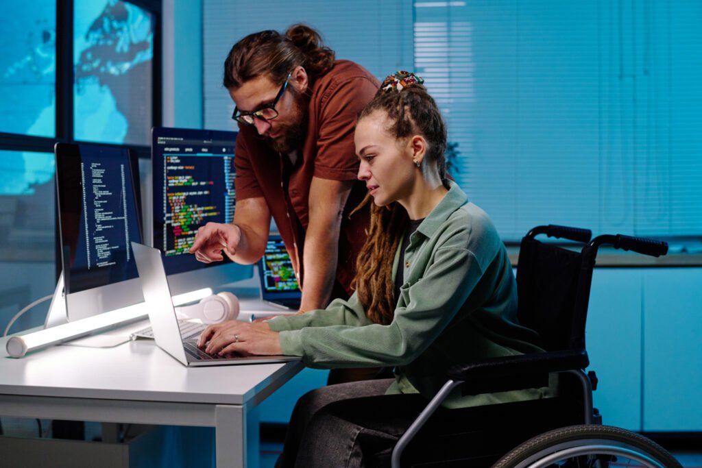 Dwie osoby, jedna na wózku inwalidzkim, patrzą na ekran komputera. WCAG 2.2 WCAG 2.1 Audyt WCAG WCAG dla początkujących.
